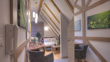 A cozy loft-style bedroom with a sloped ceiling, wooden beams, a bed, a desk, and a chair.