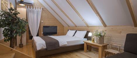 A cozy attic bedroom with a wooden bed, a television, a bedside table with a lamp, and a potted plant.