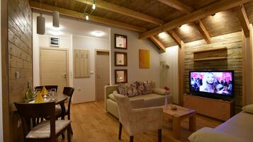 Uma sala de estar acolhedora com teto de madeira, uma área de jantar com mesa e cadeiras, um sofá e uma televisão.