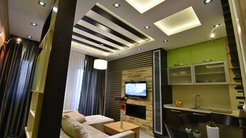 Una sala moderna con un sofá, una mesa de centro y un televisor. Hay una zona de cocina con armarios y una mesa de comedor.