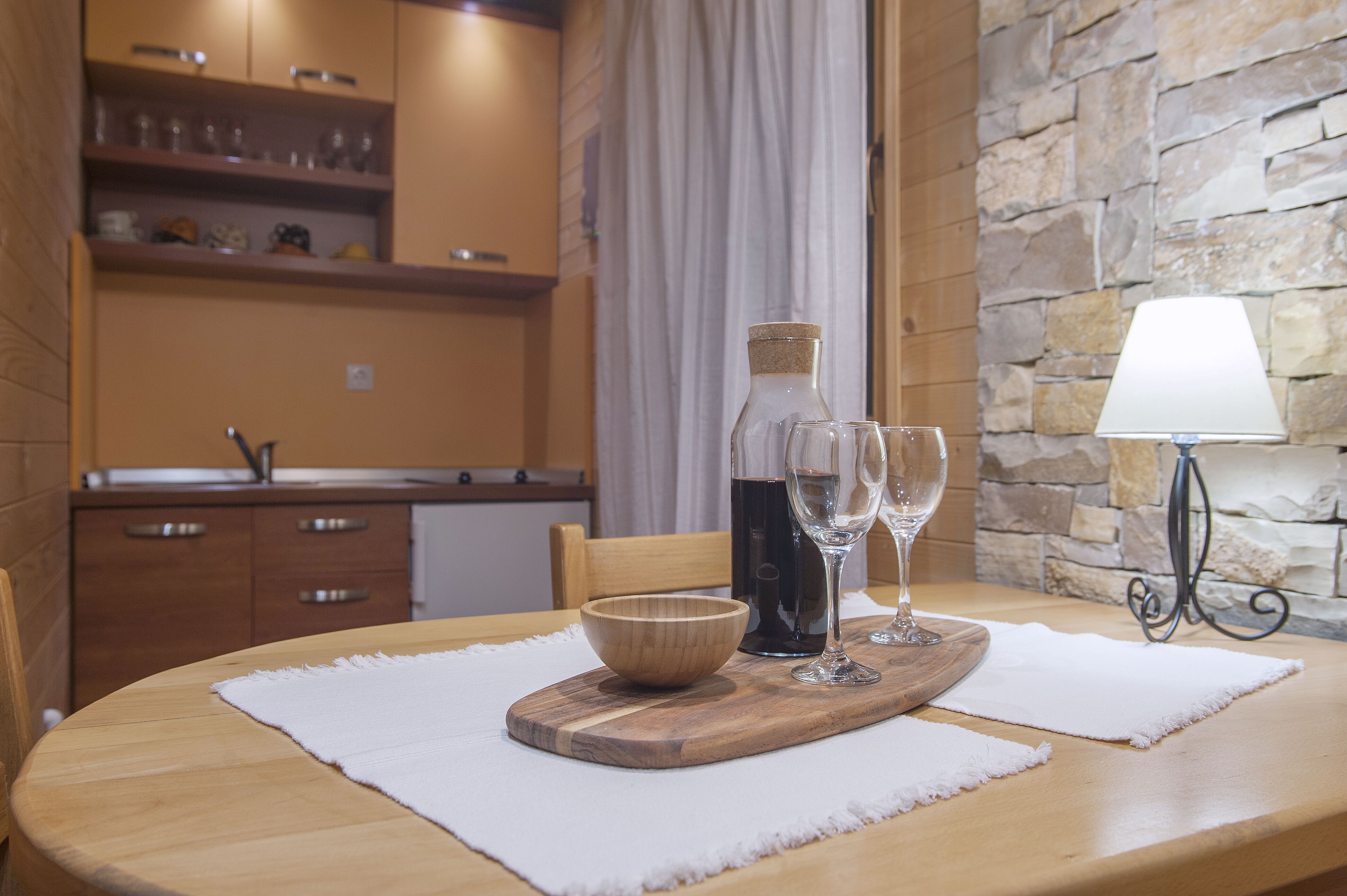Una mesa de comedor con una tabla de madera, un cuenco, una botella de vino y dos copas de vino.