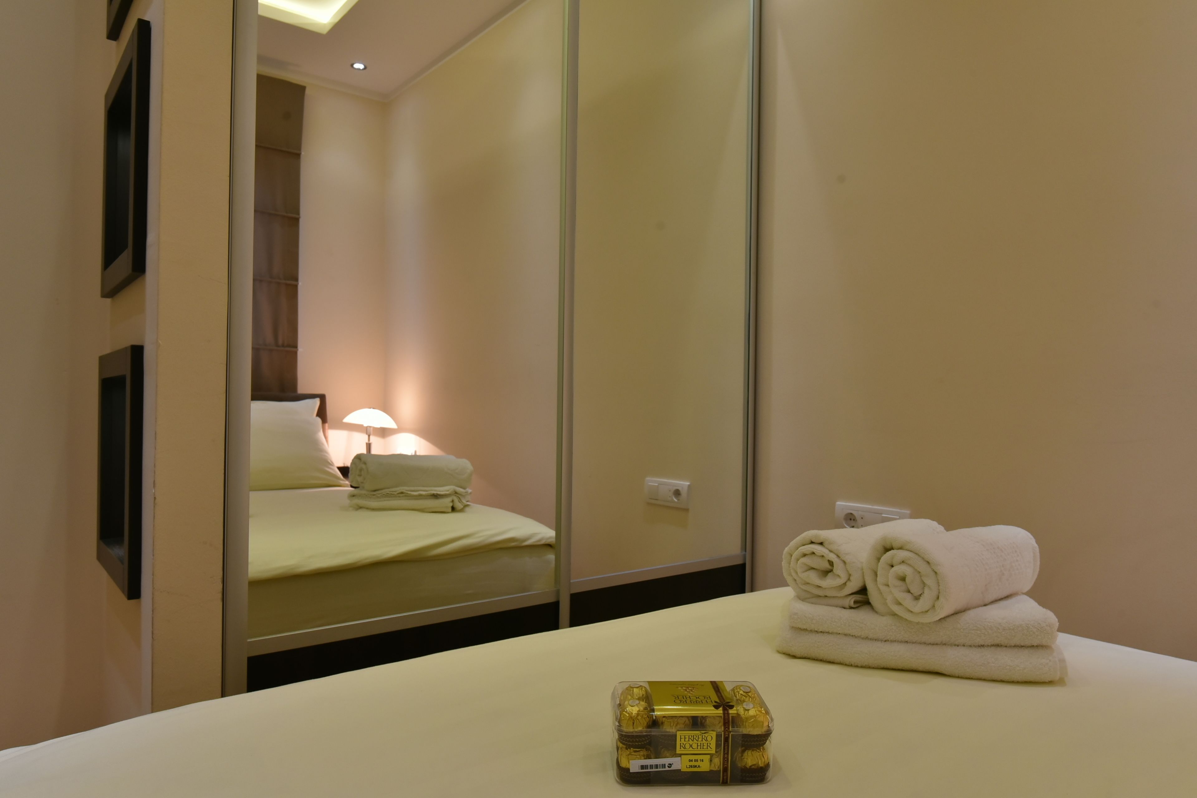 A hotel room with a bed, a mirror, and a table with towels and a bottle.