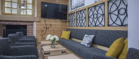 Una sala de estar moderna con chimenea, sofás grises, cojines amarillos y un televisor de pantalla plana montado en la pared.