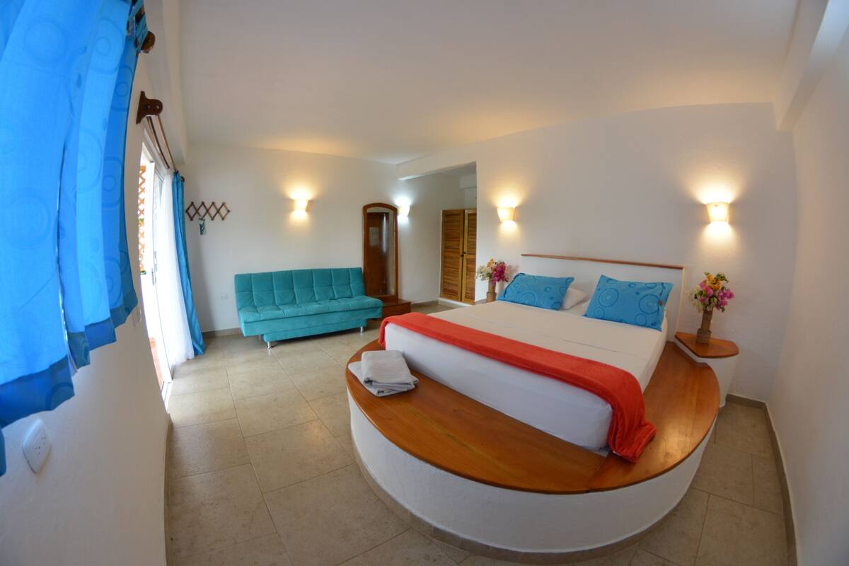 A bedroom with a bed, a sofa, and a mirror.