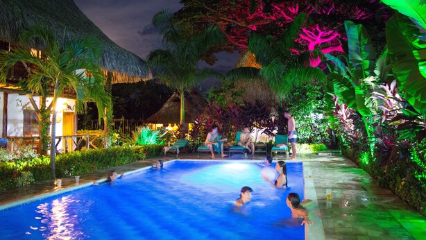 A swimming pool area with lounge chairs and a thatched-roof structure.