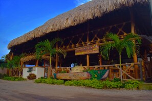 A beachside restaurant with a thatched roof and wooden structure, surrounded by palm trees and a sign reading "Primaluna Beach Hostel". - Prima Luna Palomino (Dibulla)