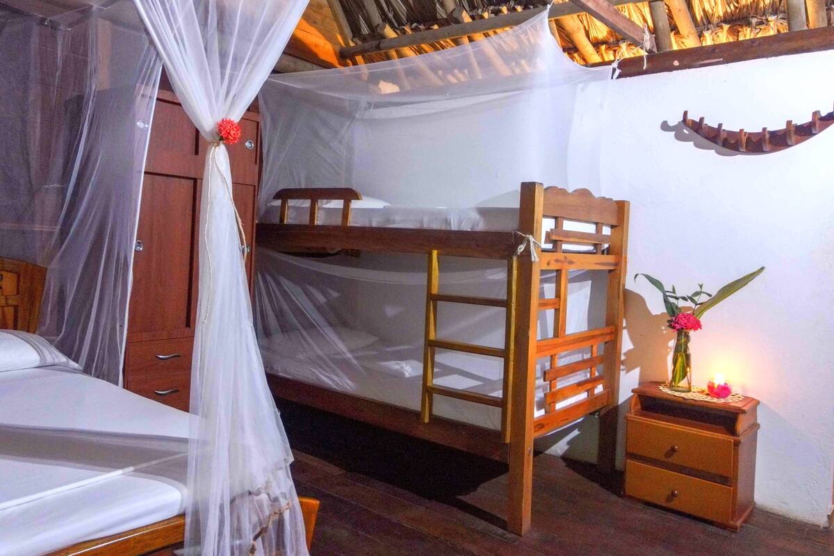A room with a bunk bed, a bedside table with a vase of flowers, and a canopy bed with mosquito netting.
