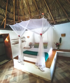 A bed with a canopy, a small table, and a wall-mounted shelf with decorative items. - Prima Luna Palomino (Dibulla)