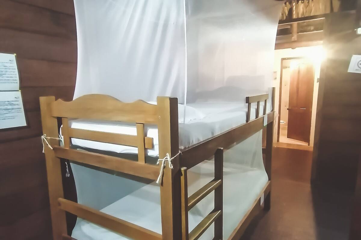 A wooden bunk bed with a mosquito net, wooden walls, and a door in the background.