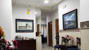 Un vestíbulo de hotel con mostrador de recepción, cuadros enmarcados en las paredes, suelo de baldosas y una escalera que conduce a otra zona.