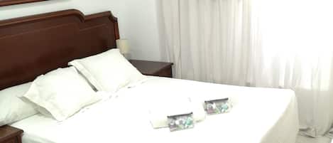 A neatly made bed with white linens, a wooden headboard, and a nightstand with a lamp.