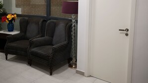 Una habitación con un sofá estampado, un jarrón con flores, una lámpara y una puerta con el número 14.
