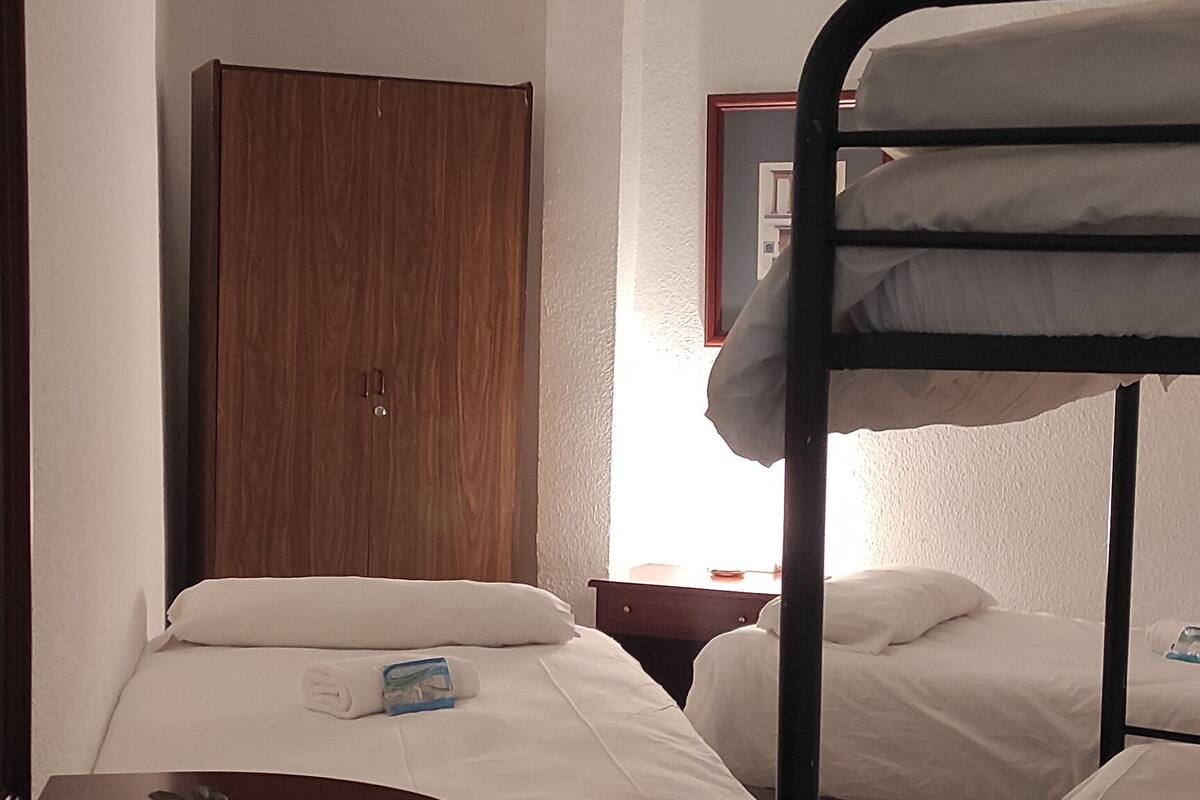 Ein Zimmer mit Etagenbetten, einem Holzschrank, einem Nachttisch mit einer Vase und einem Fenster mit Vorhängen.