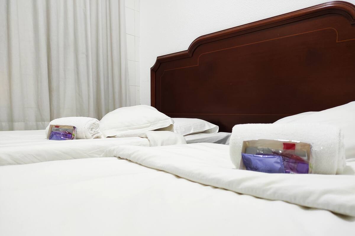 Ein Hotelzimmer mit zwei Betten, weißen Leinentüchern und ordentlich gefalteten Handtüchern.