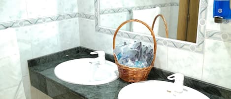 Une salle de bain avec deux lavabos, un miroir, une poubelle et un panier contenant des articles de toilette.