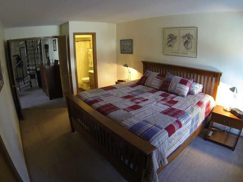 A bedroom with a wooden bed, a nightstand, a lamp, and a framed picture on the wall.