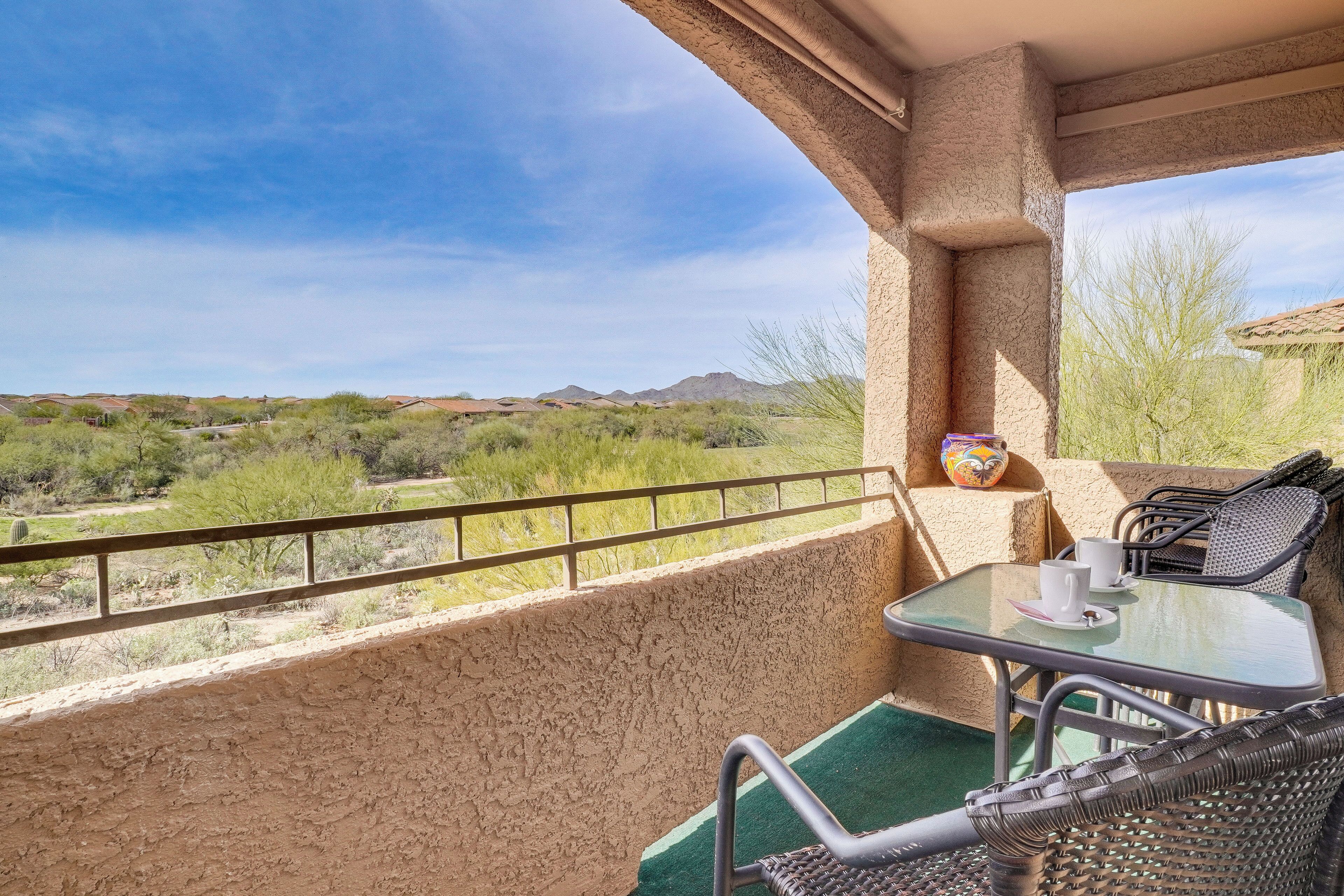 A balcony with a view of a desert landscape, a table with chairs, and a small decorative item on the wall.