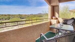 A balcony with a view of a desert landscape, a table with chairs, and a small decorative item on the wall. - Oro Valley Condo - Nearby Golf & Hiking! (Oro Valley)