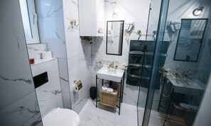 A modern bathroom with a white marble sink, a glass-enclosed shower, and a toilet.