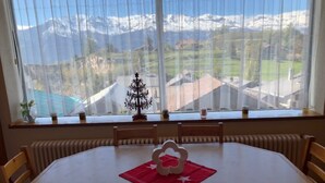 A dining table with chairs, a small Christmas tree, and a window with a view of mountains.
