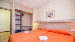 Ett hotellrum med en säng, en garderob, en vägglampa och en inramad tavla.