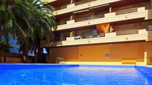 En swimmingpool med ett klart, blått vatten, omgiven av en byggnad med flera våningar och balkonger.