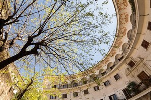 Ein Gebäude mit einer geschwungenen Fassade, mehreren Balkonen und einem Baum mit grünem Laub im Vordergrund.
