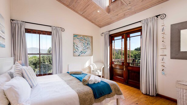 A bedroom with a large bed, a view of the outdoors, and a wooden ceiling. - House at Longbeach - upstairs apartment (Noordhoek, Chapmans Peak, Cape Town)