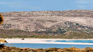 A coastal landscape with a rocky hillside and a beach. - House at Longbeach - upstairs apartment (Noordhoek, Chapmans Peak, Cape Town)