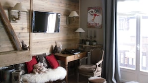 Habitació amb paret de fusta, televisió de pantalla plana, escriptori amb cadira, finestra amb cortines i un cartell a la paret.
