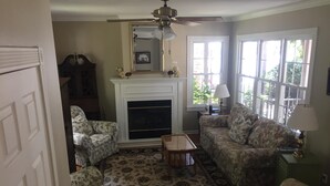 A living room with floral-patterned furniture, a fireplace, a ceiling fan, and large windows. - Guest House 632 Summit Street (Alton)