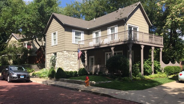 A two-story house with a stone facade, a balcony, and a front yard with a fire hydrant. - Guest House 632 Summit Street (Alton)