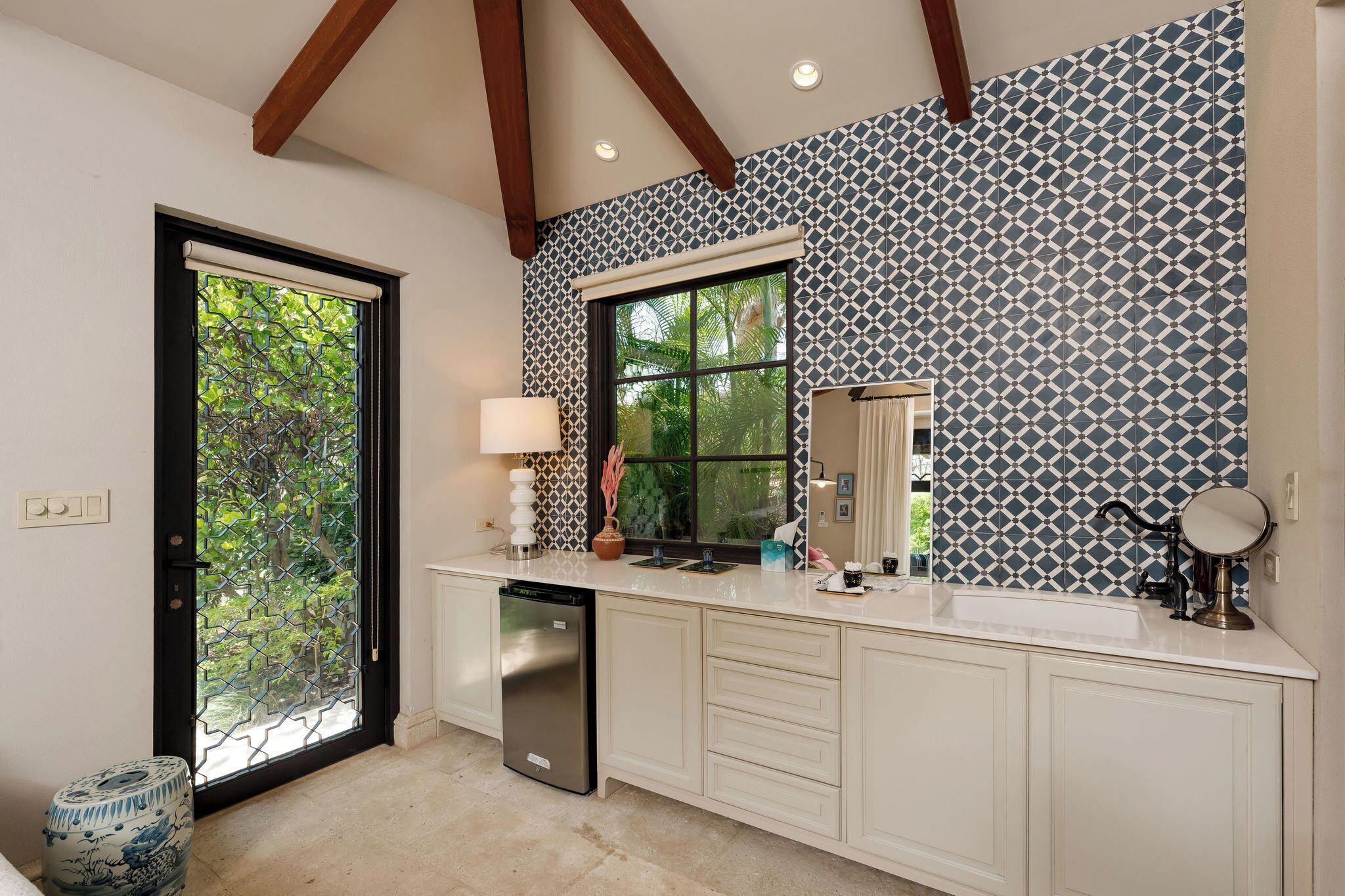 A kitchen with white cabinets, a dishwasher, a window with a view of greenery, and patterned wallpaper.