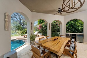 Une vaste terrasse dotée d’une table et de chaises en bois, d’une piscine et d’un ventilateur de plafond.