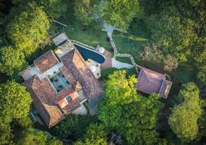 Vue aérienne d’une propriété résidentielle dotée d’une piscine, de plusieurs terrasses et d’une végétation luxuriante.