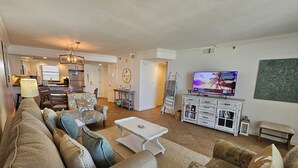 A living room with a sofa, armchairs, a coffee table, a TV, and a kitchen in the background. - Beautiful beachfront condo with Stunning Gulf Views!! 4061 BS1 (Miramar Beach)