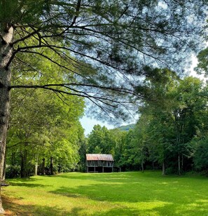 Une grange rustique se dresse au milieu d’un champ verdoyant, entourée d’une forêt dense.
