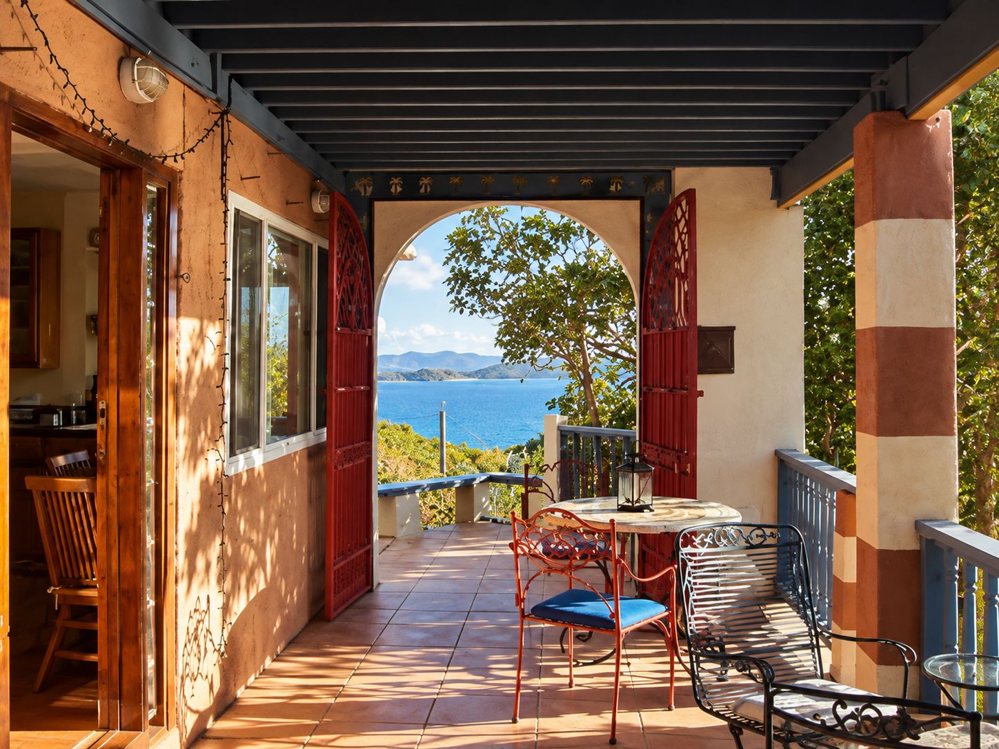 A covered outdoor area with a view of the sea, a table with chairs, and a wooden chair.