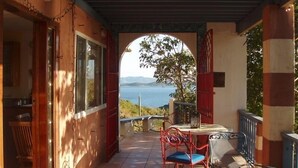 A covered outdoor area with a table and chairs, a view of the sea, and a door leading to the interior. - Lion's Gate Getaway- Lush Setting.  Check for seasonal discounts (St. Thomas,)