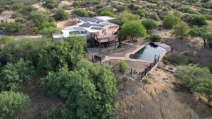 Ein Luftbild eines Hauses mit Pool, umgeben von Bäumen und einer hügeligen Landschaft.