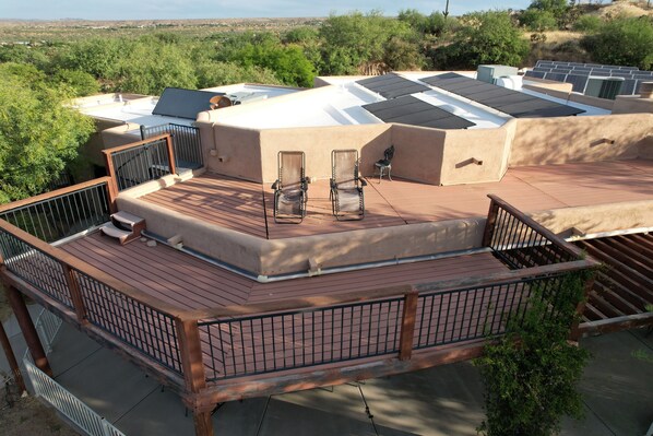 A rooftop deck with solar panels, a seating area with chairs, and a view of the surrounding landscape.