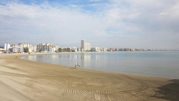 Ein Strand mit blauem Himmel, sandigem Ufer und einer Stadtkulisse im Hintergrund.