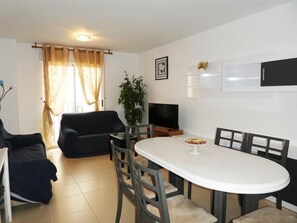 Un salon moderne avec un canapé noir, une table à manger avec des chaises, un téléviseur et une plante en pot.