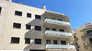 Ein mehrstöckiges Gebäude mit einer flachen Fassade, rechteckigen Fenstern und Balkonen mit Glasgeländern.