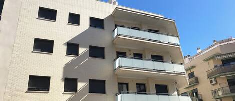A multi-story building with a flat facade, rectangular windows, and balconies with glass railings.