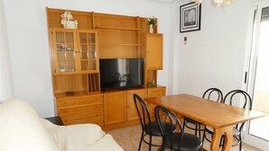 Ein kompakter Wohnbereich mit Sofa, Esstisch, Stühlen, Fernseher, Holzschränken und einem kleinen dekorativen Gegenstand auf dem Schrank.