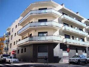 Un immeuble résidentiel à plusieurs étages, doté de balcons, d’un panneau indiquant l’interdiction d’accès et de voitures garées.
