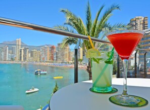 A table with two drinks and a view of a beach and cityscape. - Lido (Benidorm)