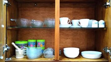 Un meuble en bois doté d’étagères en verre, dans lequel sont rangés divers ustensiles de cuisine.