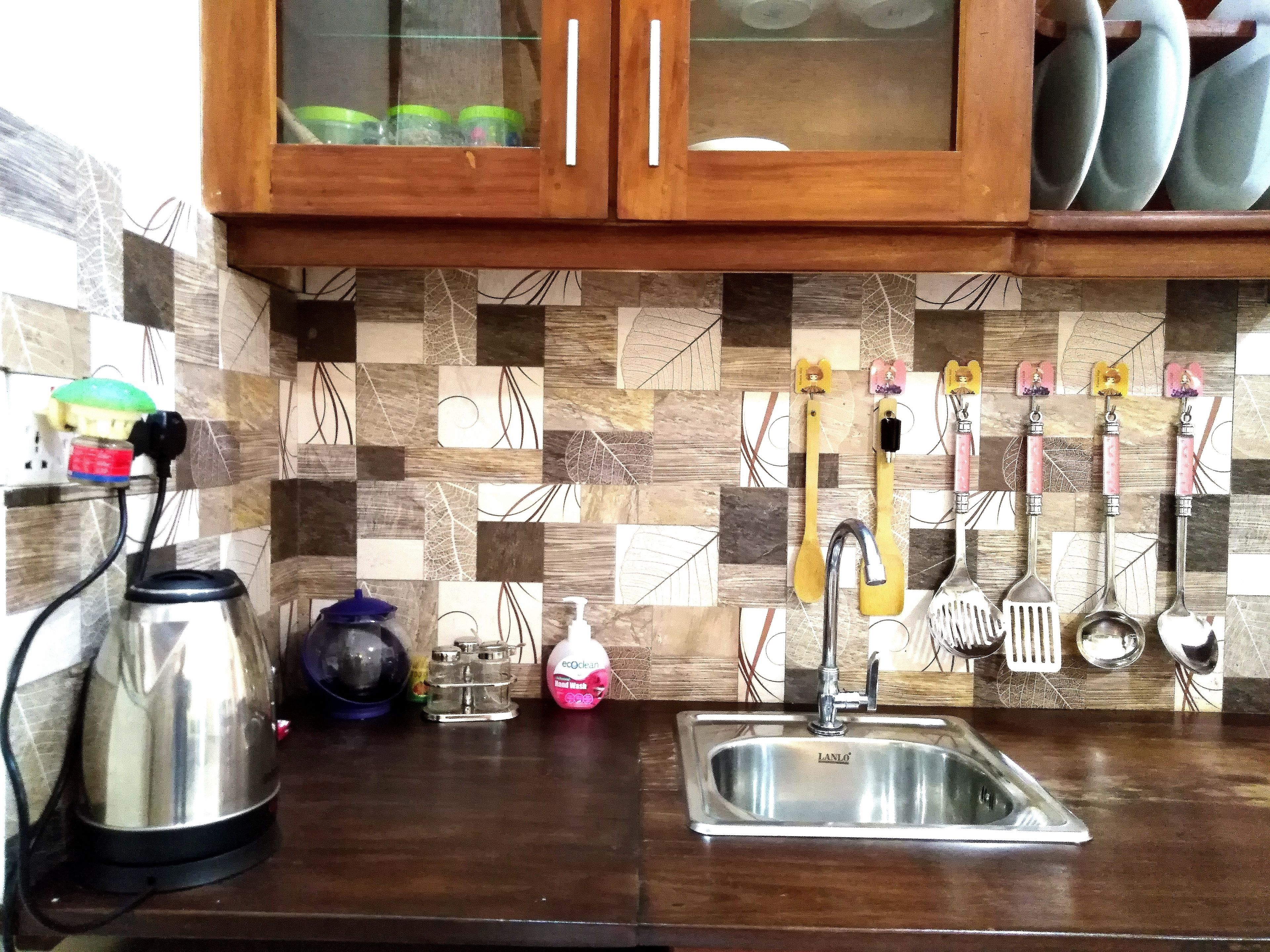 A kitchen with a stainless steel sink, wooden cabinets, and a checkered backsplash.